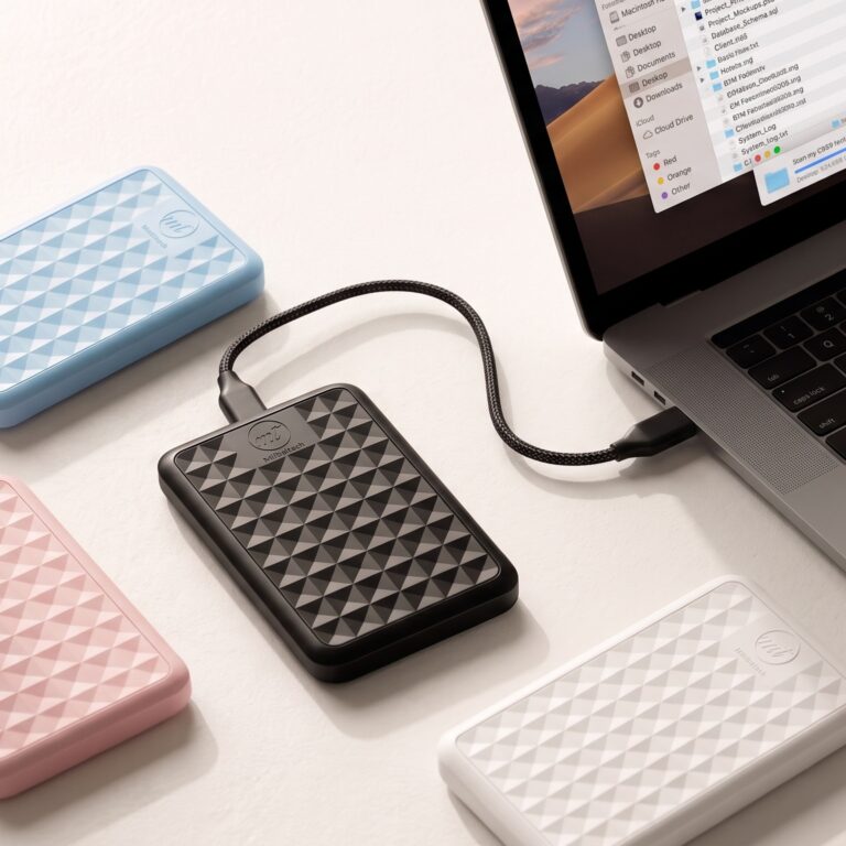 Black ModusTech Facet portable hard drive plugged into a laptop, with blue, pink and white Facet drives beside it